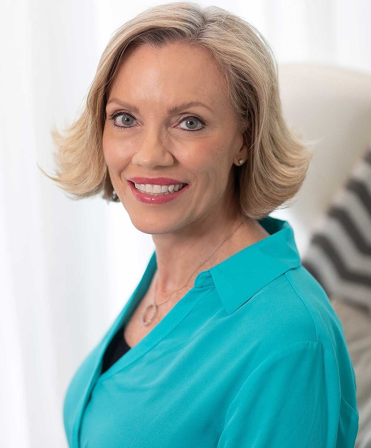 Smiling woman in turquoise blouse, indoors.