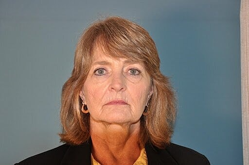 Woman with short hair, serious expression, blue background.