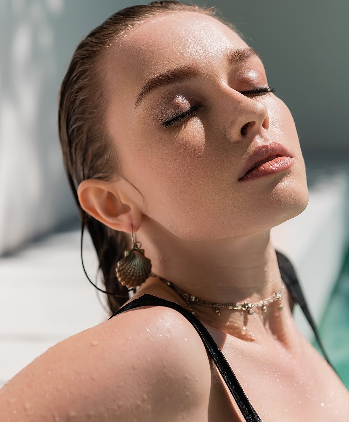 Person with closed eyes near water, sunlight glow.