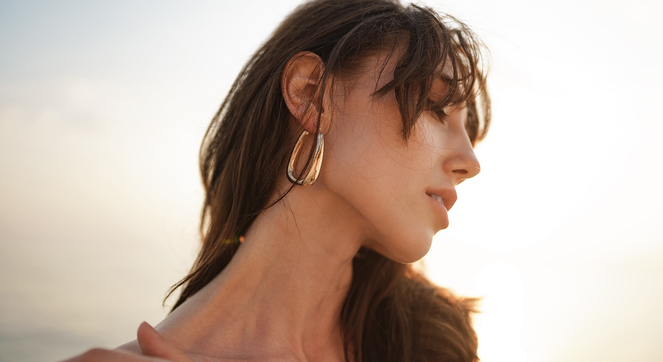 Profile of a woman with earrings at sunset.