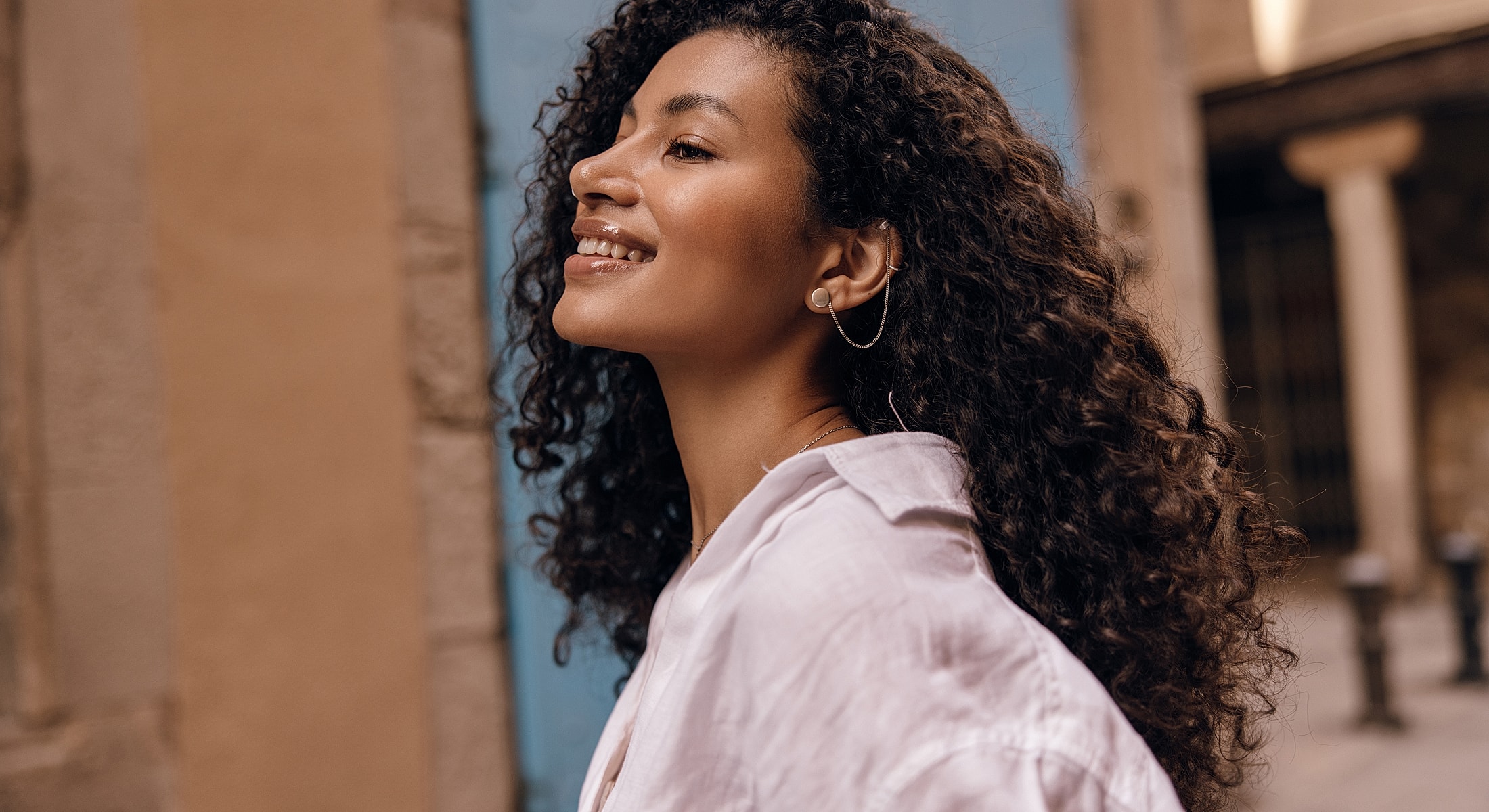 Smiling woman with curly hair in urban setting.