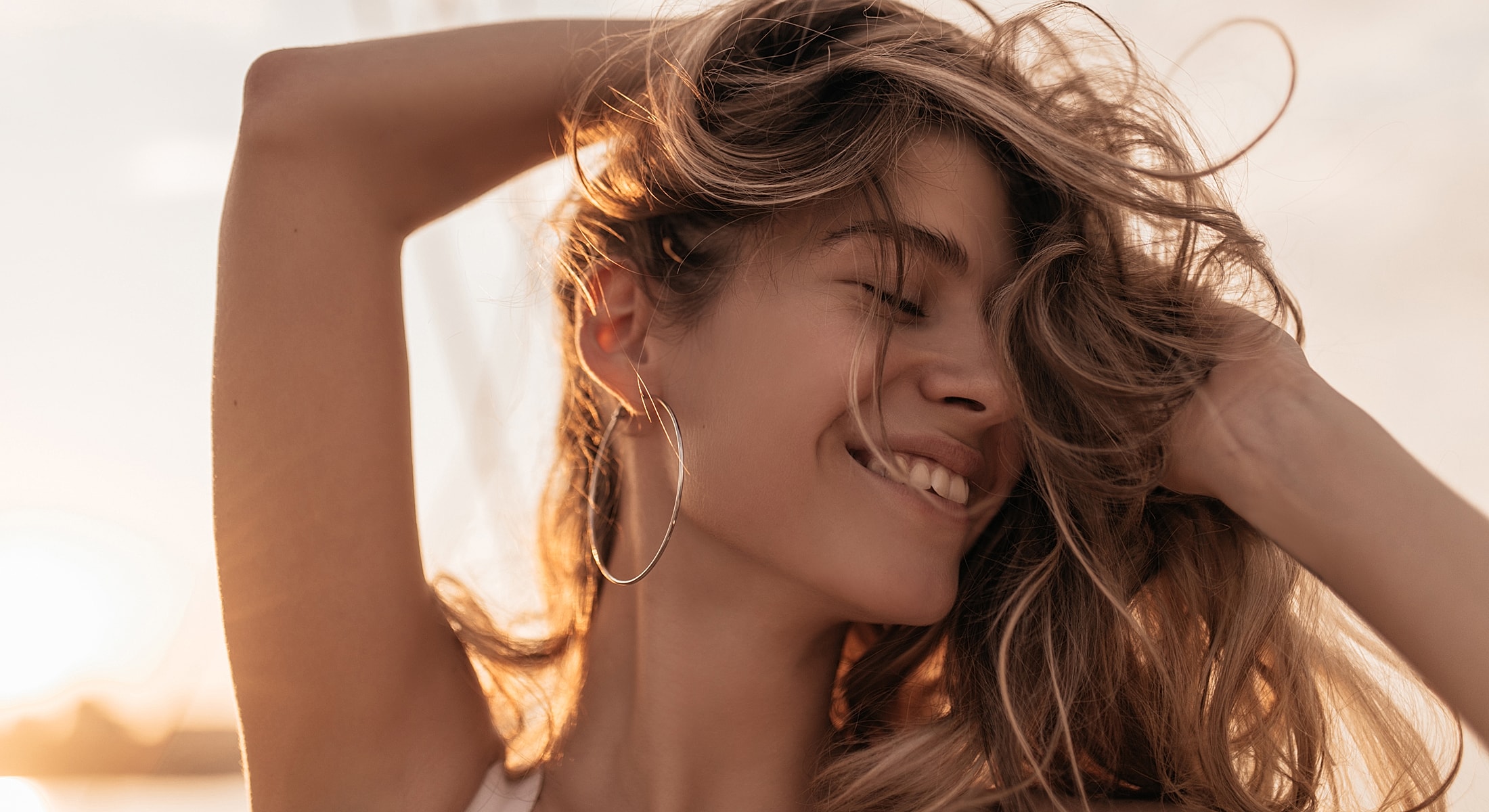 Woman smiling with wind-swept hair at sunset.
